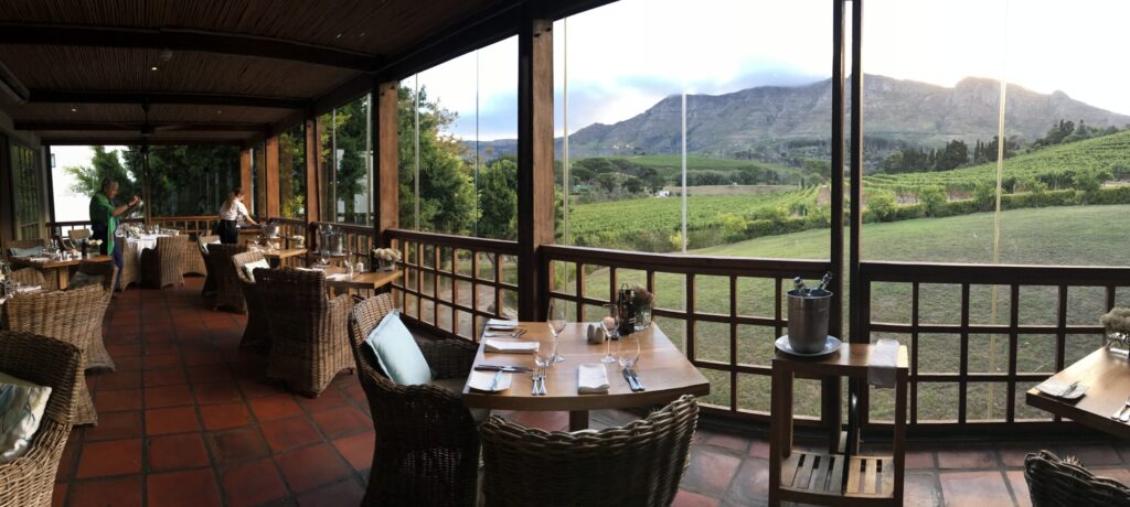 Überdachte Terrasse mit gedeckten Tischen und Blick über Weinberge auf die Berge